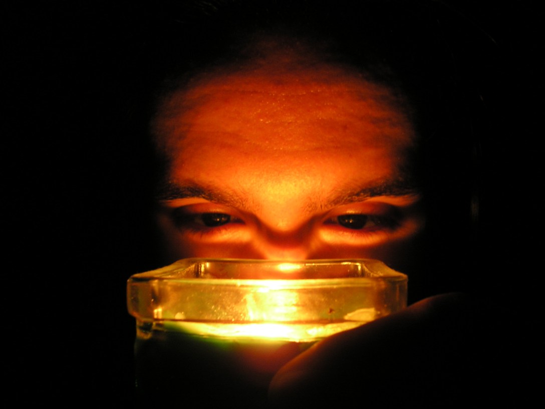 Art's face lit from below by a candle in a dark room.